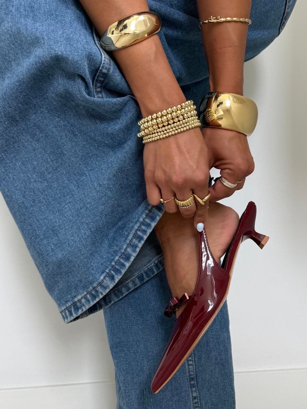 Stacked gold bangles and rings styled with burgundy patent kitten heels